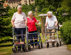 Drei Damen spazieren mit ihren Rollatoren durch den schönen Garten des Hauses.