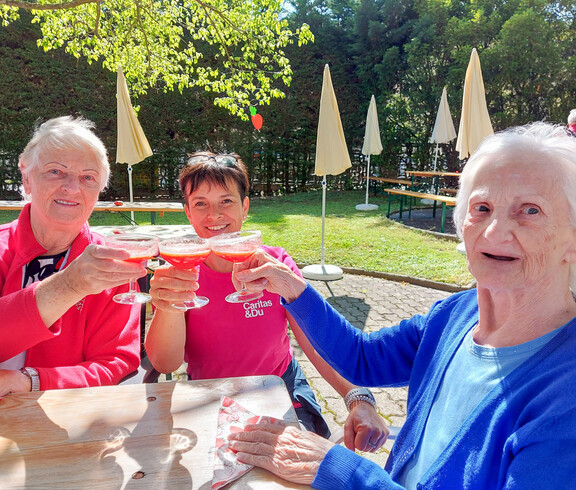 Bewohnerinnen und eine Betreuerin vom Haus Elisabeth genießen ein Erdbeergetränk beim Erdbeerfest. Sie sitzen im Freien an einen Tisch und es ist schönes Wetter