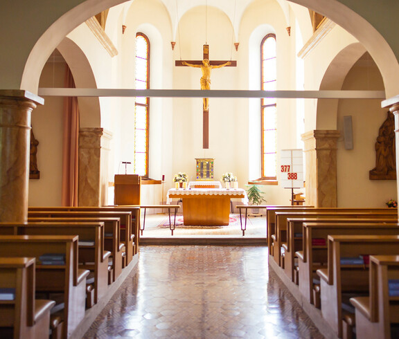 Die Kappele mit Kirchenbänken rechts und links, sowie den Altar in der Mitte. Über diesem hängt ein großes Kreuz.