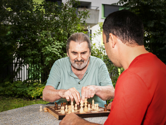 älterer Mann spielt Schach mit Caritas Mitarbeiter