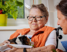 Eine Bewohnerin hält ein dreifärbiges Meerschweinchen auf dem Arm.