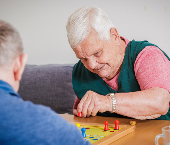 Eine Bewohnerin spielt mit einem Bewohner "Mensch ärgere dich nicht".