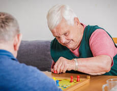 Eine Bewohnerin spielt mit einem Bewohner "Mensch ärgere dich nicht".