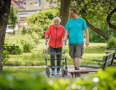 Eine ältere Dame begleitet von einem Pfleger gehen im Garten spazieren.