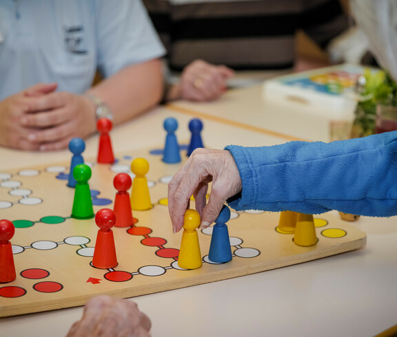 Bewohner*innen spielen gemeinsam mit einer Betreuerin "Mensch ärgere dich nicht".