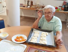 Ältere Dame sitzt am Tisch und befüllt Teigtaschen.