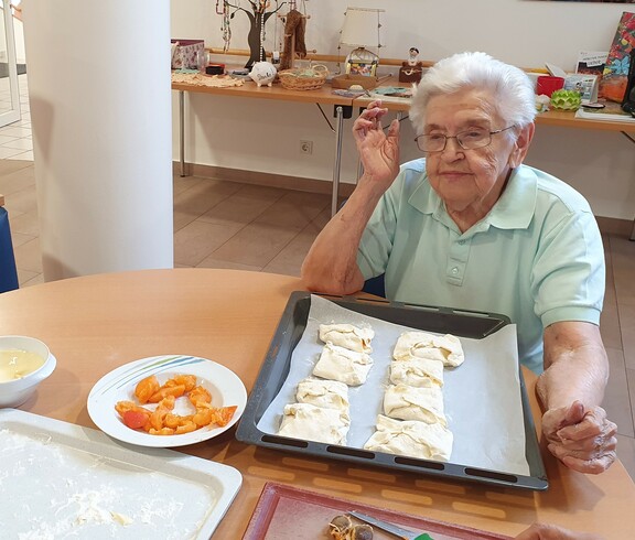 Ältere Dame sitzt am Tisch und befüllt Teigtaschen.