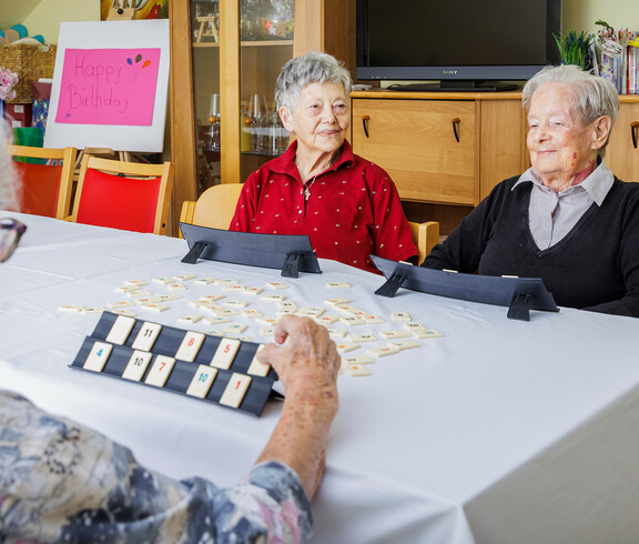 Drei Bewohnerinnen sitzen am Tisch und spielen Rummikub.