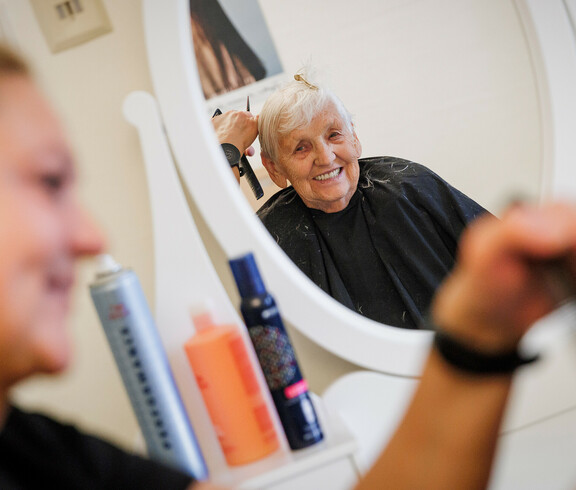 Im Spiegel sieht man eine glückliche Dame, der gerade die Haare geschnitten werden.