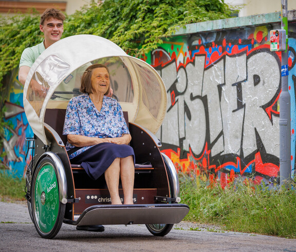 Ein Zivildiener fährt mit der Rikscha des Hauses, in der eine Bewohnerin sitzt in die Stadt. 