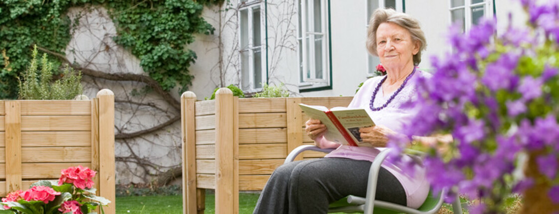 Bewohnerin beim Lesen im Garten