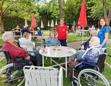 Man sieht die Bewohnerinnen des Haus Elisabeth mit Betreuerinnen. Sie genießen an einen Tisch im Freien das Erbeerfest. Es steht Erdbeerkuchen am Tisch