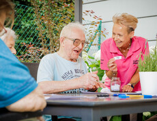 Eine Betreuerin hält einen Zettel mit der Zahl 70 hoch, ein Bewohner kreuzt auf seinem Bingo-Zettel diese Zahl ab.