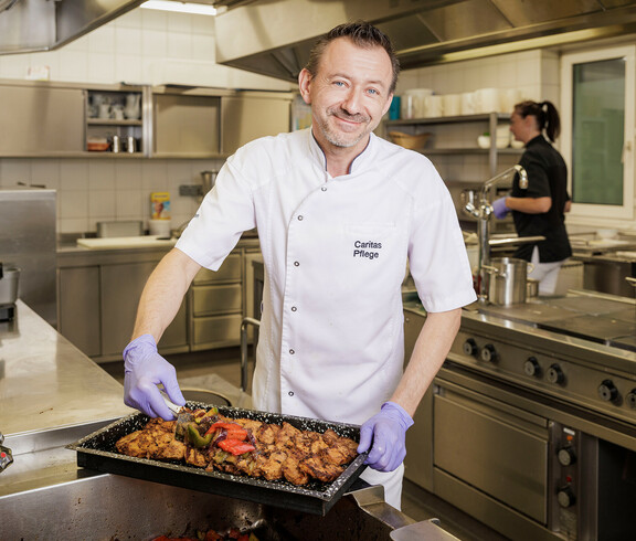 Der Koch des Hauses lächelt, während er ein Blech mit frisch gekochten Essen würzt.