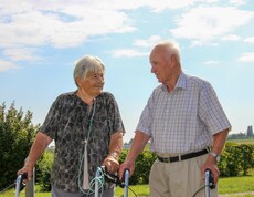 Zwei Personen aus dem Haus Lisa steht mit Rollatoren im Freien und unterhält sich. Die Frau hat eine Sauerstoffnasenbrille, und beide genießen den sonnigen Tag in einer ländlichen Umgebung.