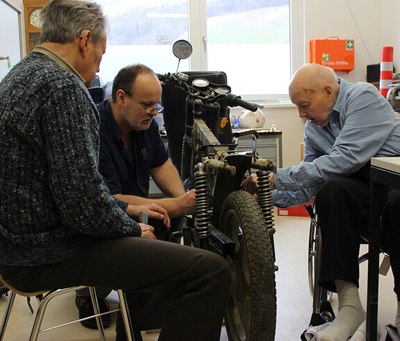 Tagesgast Otmar Schober, Haustechniker Georg Ponzer und Bewohner Fritz Brandl werkeln am Motorrad in der Werkstatt