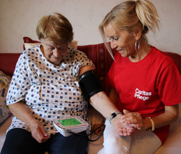 Caritas Mitarbeiterin der Hauskrankenpflege misst Blutdruck bei Klientin