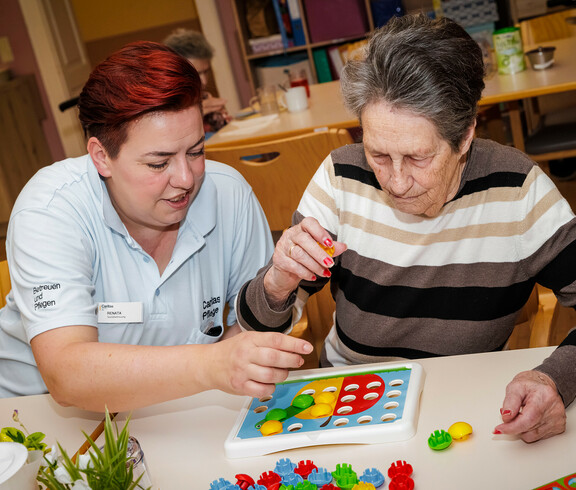 Eine Bewohnerin und eine Pflegerin sitzen vor einem Koordinations-Puzzel und lösen es gemeinsam.