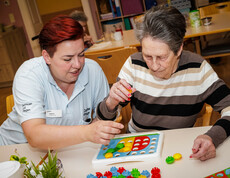 Eine Bewohnerin und eine Pflegerin sitzen vor einem Koordinations-Puzzel und lösen es gemeinsam.