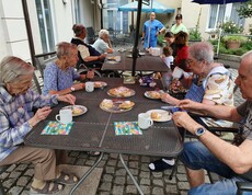 Gruppe älterer Leute sitzt beim Tisch im Garten bei Kaffee und Kuchen.