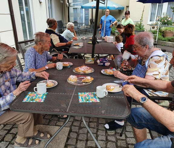 Gruppe älterer Leute sitzt beim Tisch im Garten bei Kaffee und Kuchen.