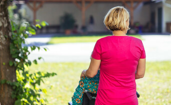 Eine ältere Dame mit weißen Harren und gelben Pullover sieht eine Pflegekraft an, die sie anlächelt.