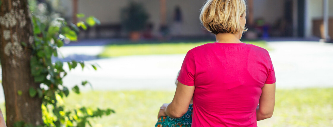 Eine ältere Dame mit weißen Harren und gelben Pullover sieht eine Pflegekraft an, die sie anlächelt.