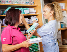 Zwei Mitarbeiter*innen stellen die Tabletten für die Bewohner*innen zusammen und lächeln sich an.