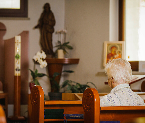 Eine Dame sitzt auf einer Kirchenbank mit dem Rücken zugekehrt und betet in der hauseigenen Kapelle.