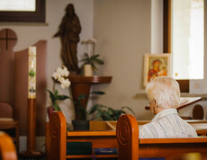 Eine Dame sitzt auf einer Kirchenbank mit dem Rücken zugekehrt und betet in der hauseigenen Kapelle.