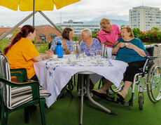 Eine Gruppe von Bewohnerinnen sitzt gemeinsam mit zwei Pflegerinnen bei einer Tasse Kaffee auf der Dachterrasse des Haues. 