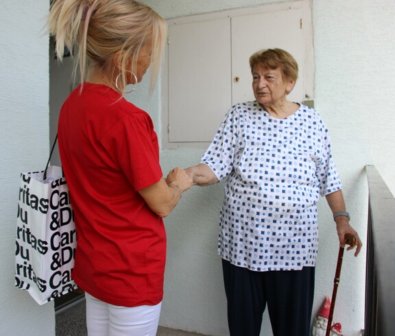 Caritas Mitarbeiterin der Hauskrankenpflege begrüßt Klientin zuhause