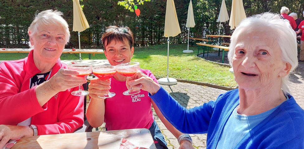 Bewohnerinnen und eine Betreuerin vom Haus Elisabeth genießen ein Erdbeergetränk beim Erdbeerfest. Sie sitzen im Freien an einen Tisch und es ist schönes Wetter